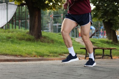Photo of Athletic young man in sportswear running outdoors, closeup. Space for text