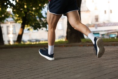 Photo of Athletic young man in sportswear running outdoors, closeup