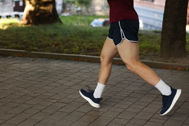 Photo of Athletic young man in sportswear running outdoors, closeup. Space for text