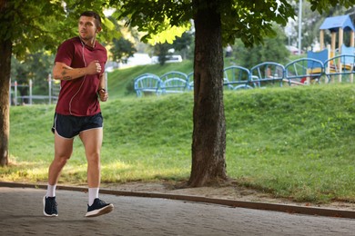 Photo of Athletic young man in sportswear running outdoors, space for text