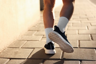 Photo of Athletic young man in sportswear running outdoors, closeup. Space for text