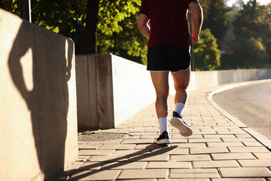 Photo of Athletic young man in sportswear running outdoors, closeup