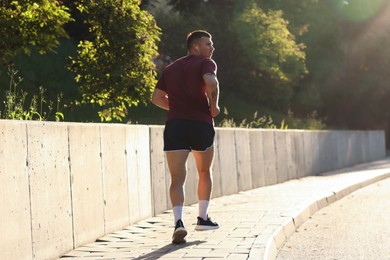 Photo of Athletic young man in sportswear running outdoors, back view