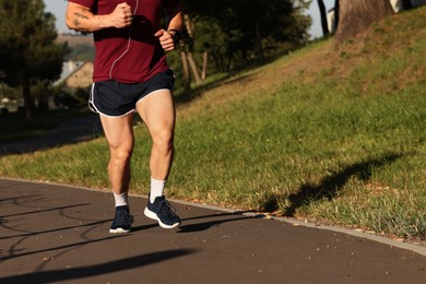 Photo of Athletic young man in sportswear running outdoors, closeup. Space for text