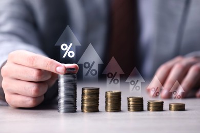 Image of Man stacking coins at table, closeup. Percent signs and arrows above stacks