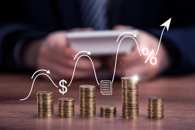 Image of Arrow with percent sign and icons above stacked coins on wooden table. Man using calculator, selective focus