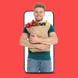 Image of Delivery service worker giving online order out of mobile phone against red background. Man with paper bag full of food products