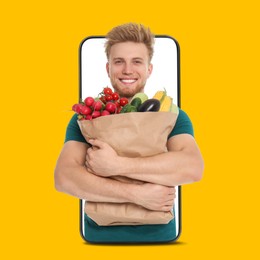 Image of Delivery service worker giving online order out of mobile phone against orange background. Man with paper bag full of food products