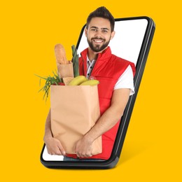 Image of Delivery service worker giving online order out of mobile phone against orange background. Man with paper bag full of food products