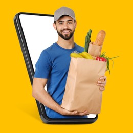Image of Delivery service worker giving online order out of mobile phone against orange background. Man with paper bag full of food products