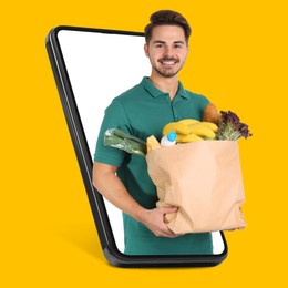 Image of Delivery service worker giving online order out of mobile phone against orange background. Man with paper bag full of food products