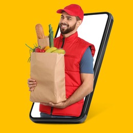 Image of Delivery service worker giving online order out of mobile phone against orange background. Man with paper bag full of food products