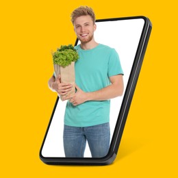 Image of Delivery service worker giving online order out of mobile phone against orange background. Man with paper bag full of food products