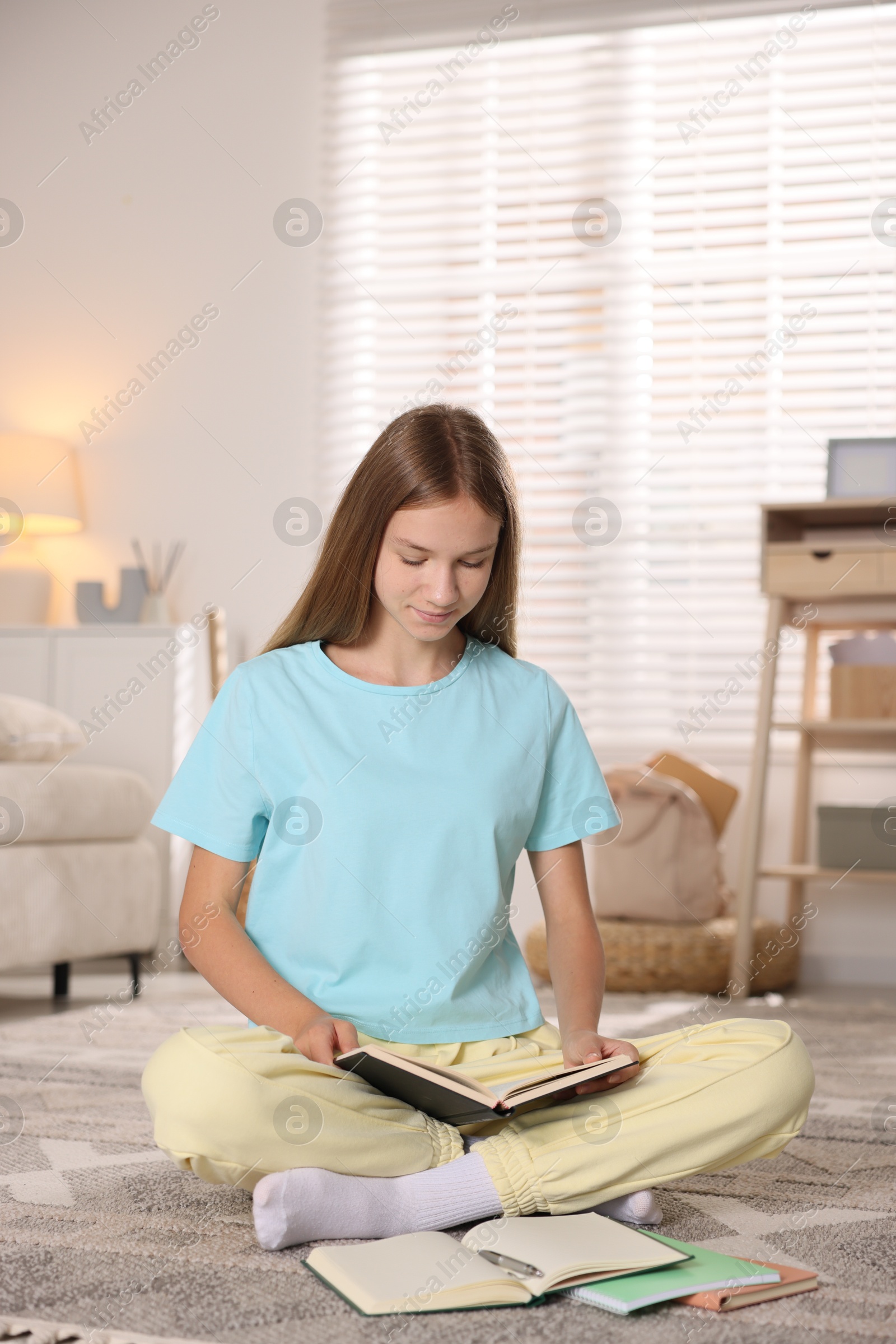 Photo of Teenage girl studying with books on floor at home