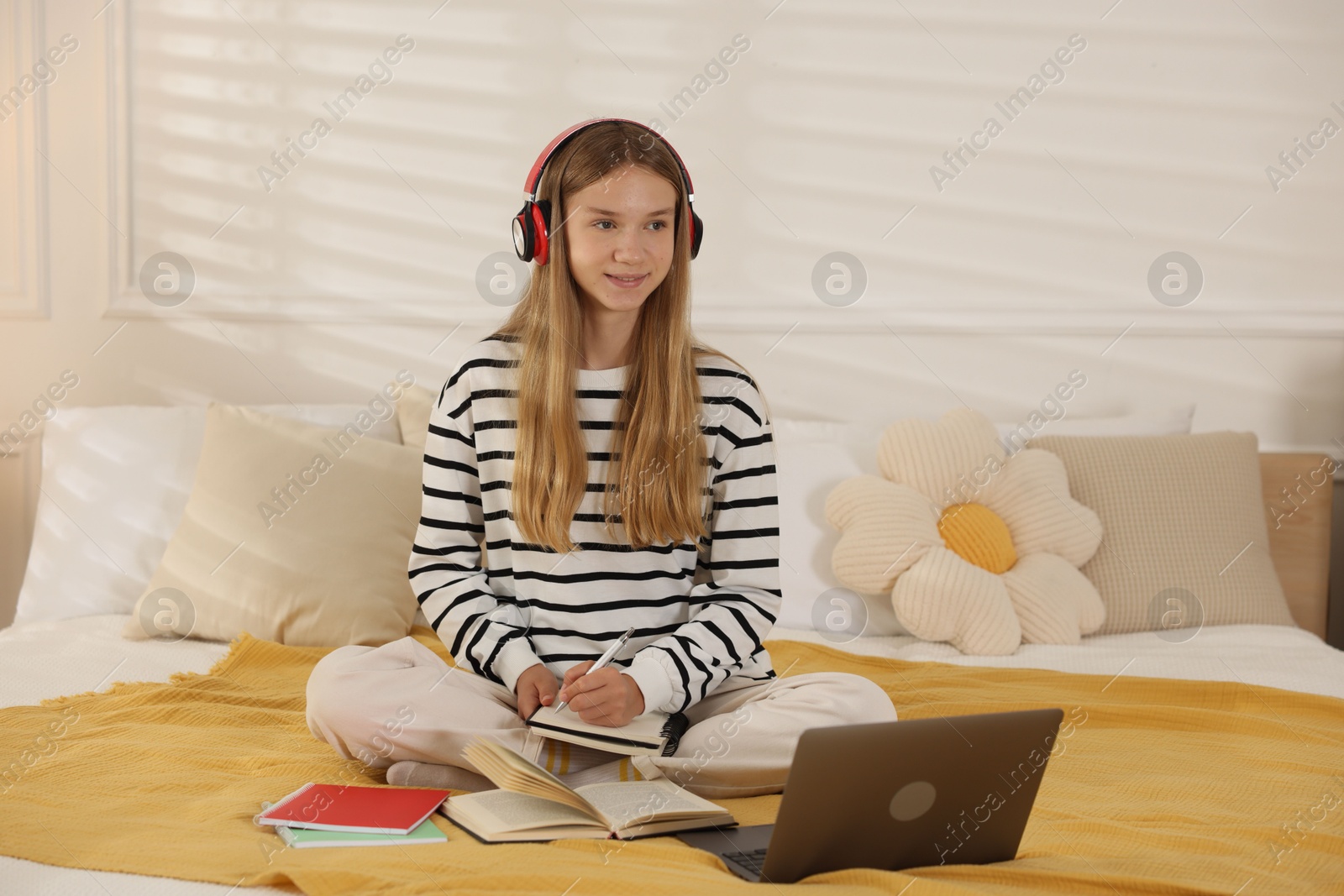Teenage girl in headphones studying online on bed at home Photo of Teenage girl in headphones studying online on bed at home