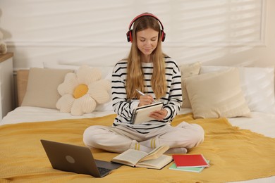 Photo of Teenage girl in headphones studying online on bed at home