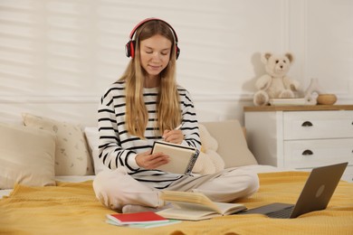 Photo of Teenage girl in headphones studying online on bed at home