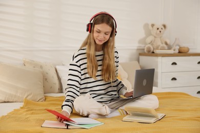 Photo of Teenage girl in headphones studying online on bed at home