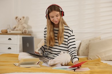 Photo of Teenage girl in headphones studying online on bed at home