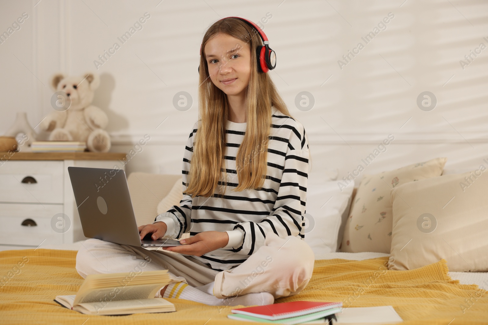 Teenage girl in headphones studying online on bed at home Photo of Teenage girl in headphones studying online on bed at home