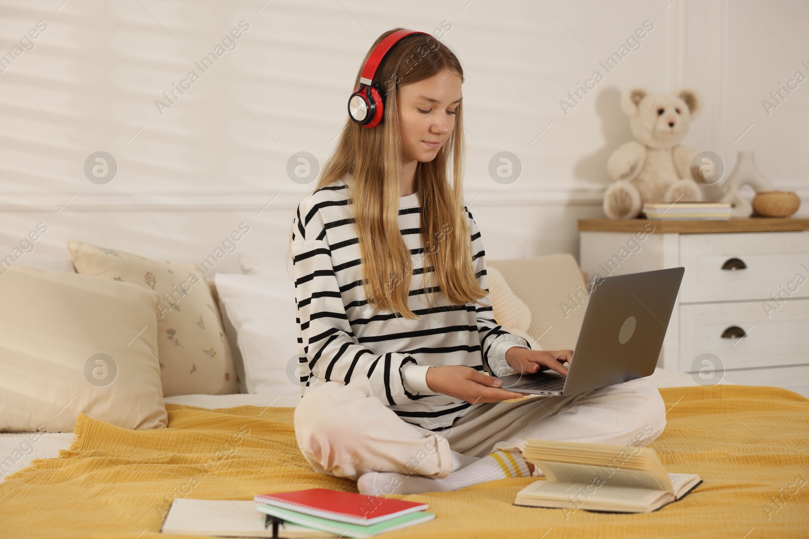 Teenage girl in headphones studying online on bed at home Photo of Teenage girl in headphones studying online on bed at home