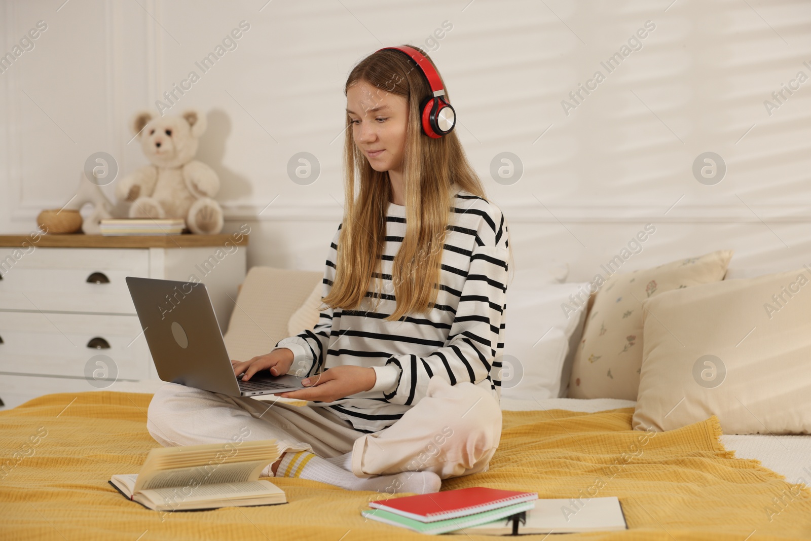 Teenage girl in headphones studying online on bed at home Photo of Teenage girl in headphones studying online on bed at home