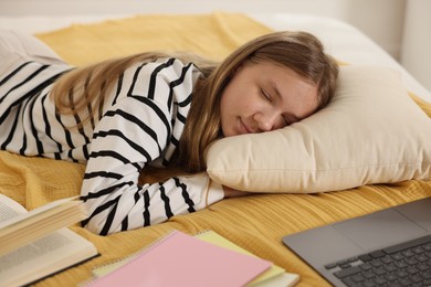 Photo of Tired teenage student sleeping near laptop and notebooks on bed at home