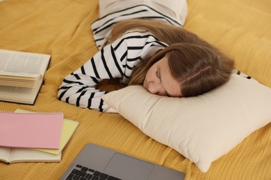 Photo of Tired teenage student sleeping near laptop and notebooks on bed at home