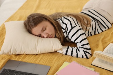 Photo of Tired teenage student sleeping near laptop and notebooks on bed at home