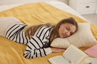 Photo of Tired teenage student sleeping near books on bed indoors