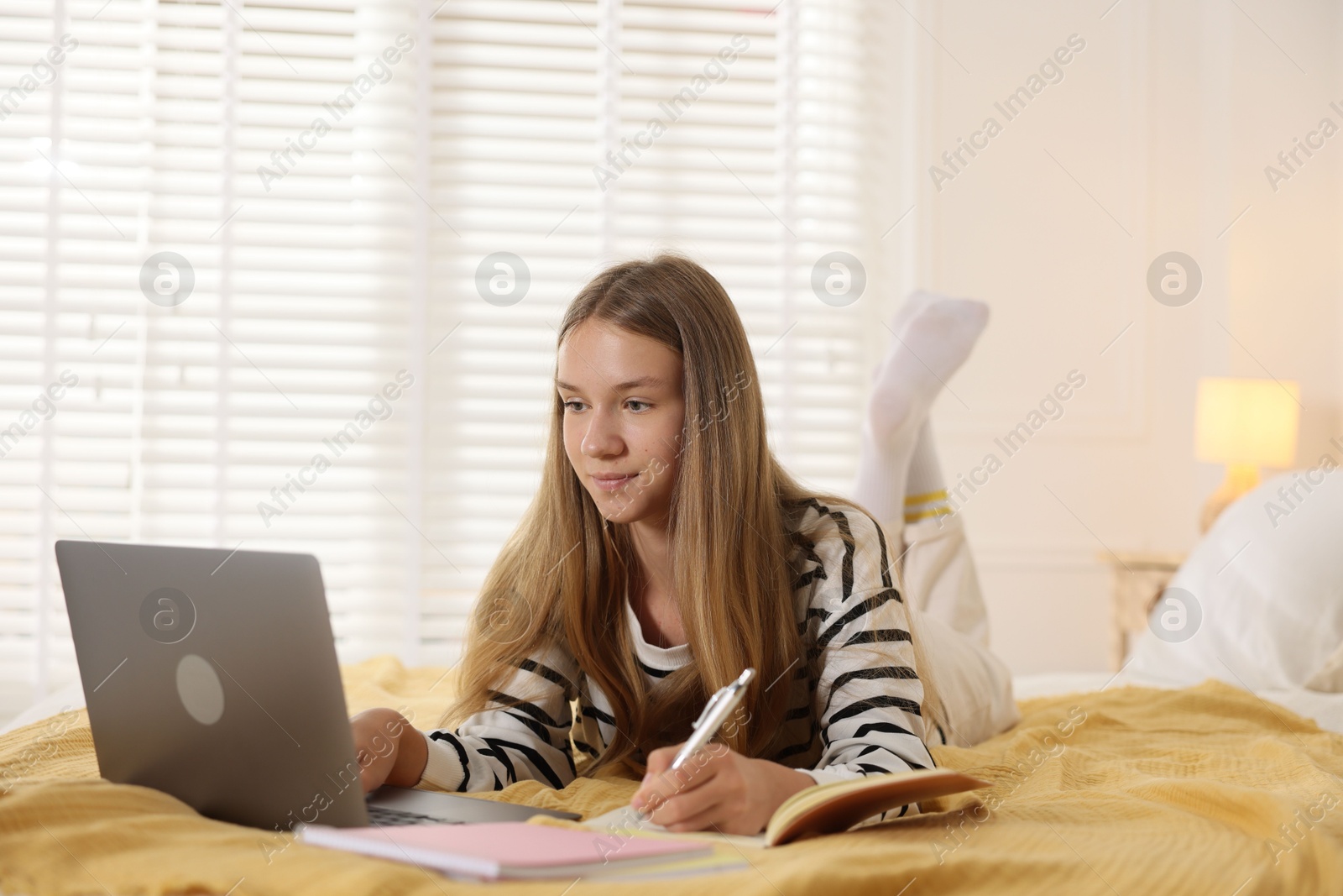 Photo of Teenage girl studying online with laptop on bed at home