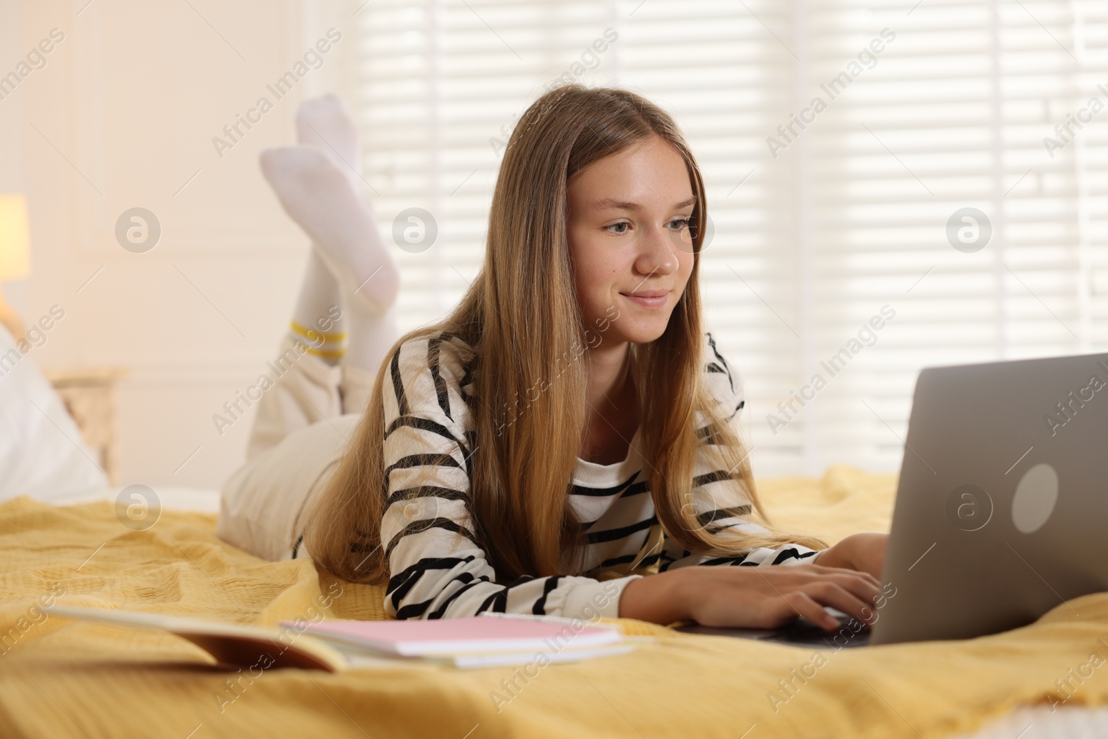 Photo of Teenage girl studying online with laptop on bed at home