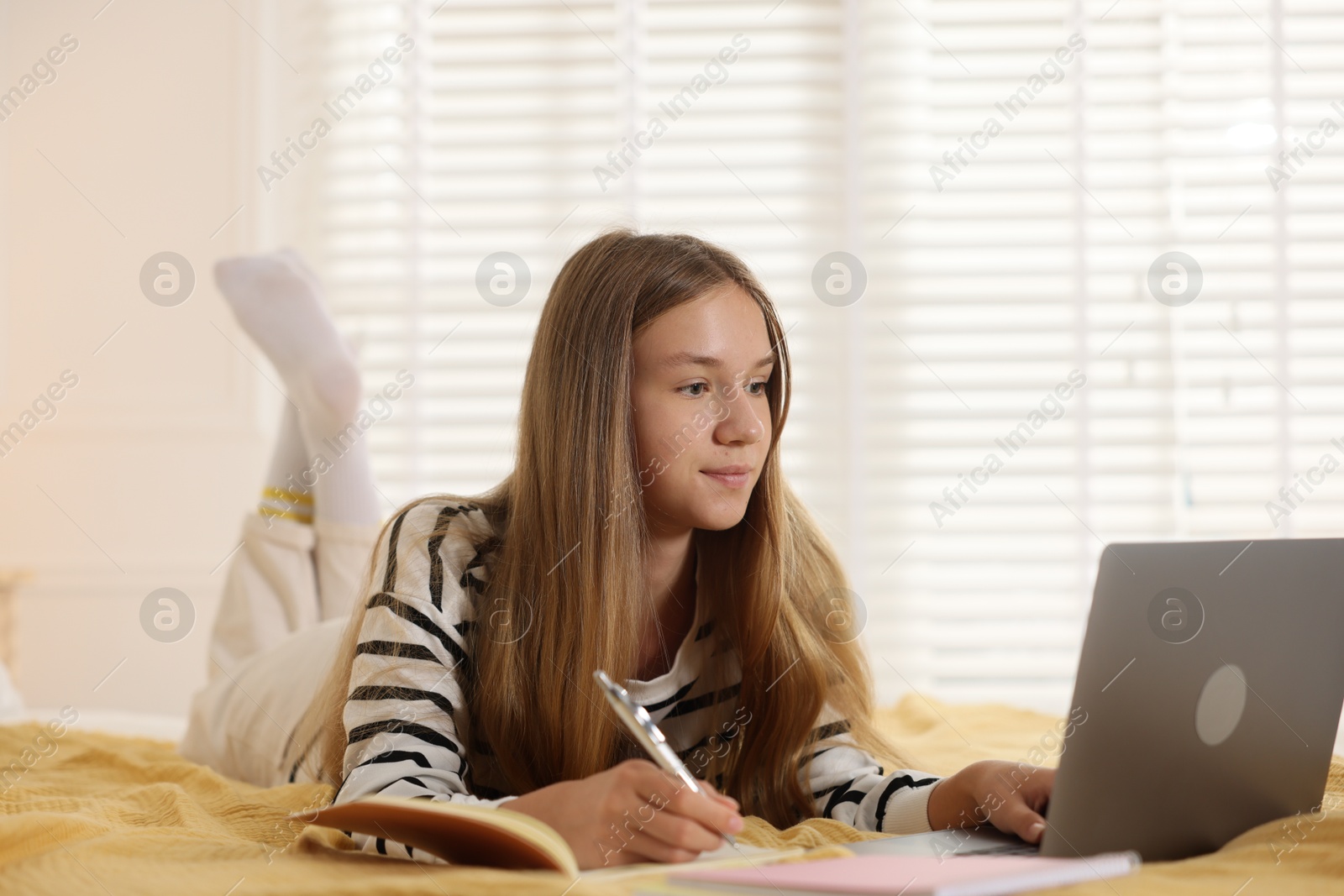 Teenage girl studying online with laptop on bed at home Photo of Teenage girl studying online with laptop on bed at home