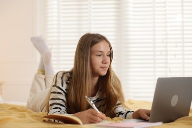 Photo of Teenage girl studying online with laptop on bed at home