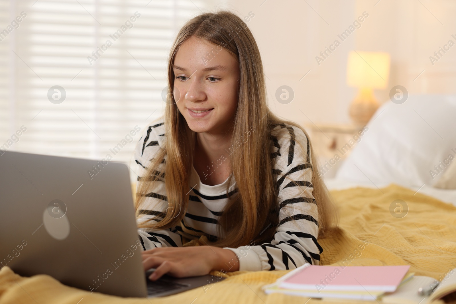 Teenage girl studying online with laptop on bed at home Photo of Teenage girl studying online with laptop on bed at home