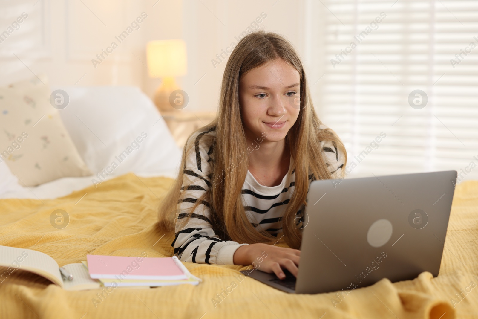 Teenage girl studying online with laptop on bed at home Photo of Teenage girl studying online with laptop on bed at home