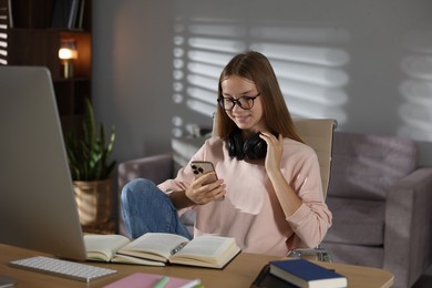 Photo of Studying online. Teenage girl using smartphone at table indoors