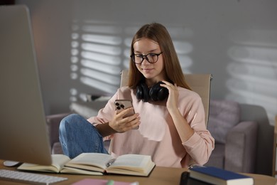 Photo of Studying online. Teenage girl using smartphone at table indoors