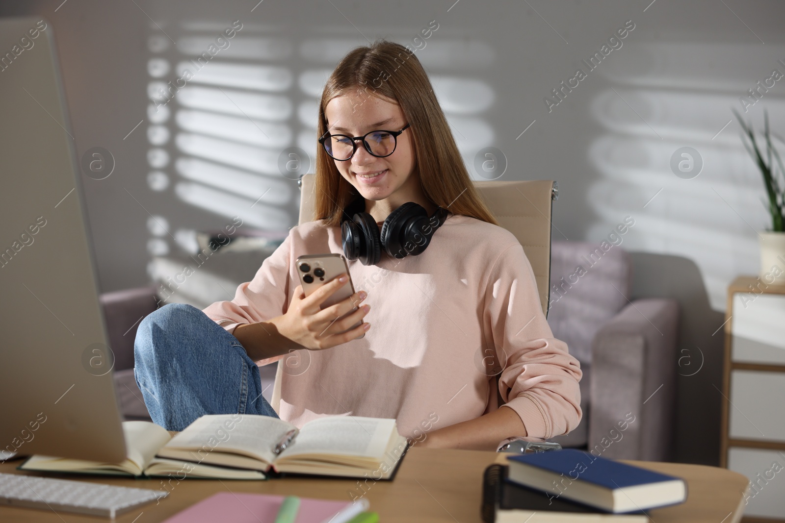 Studying online. Teenage girl using smartphone at table indoors Photo of Studying online. Teenage girl using smartphone at table indoors