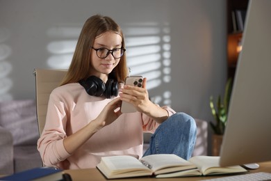Photo of Studying online. Teenage girl using smartphone at table indoors