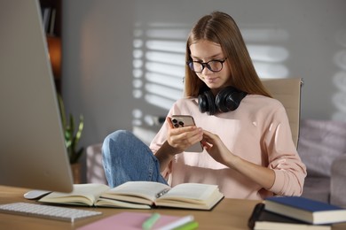 Photo of Studying online. Teenage girl using smartphone at table indoors