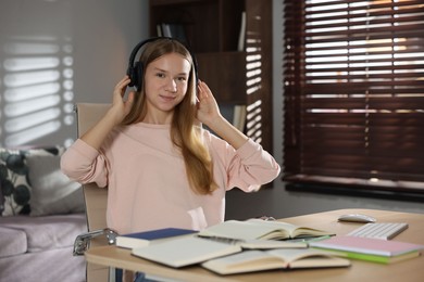 Photo of Teenage girl in headphones studying online at table indoors