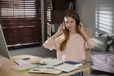 Photo of Teenage girl in headphones studying online at table indoors