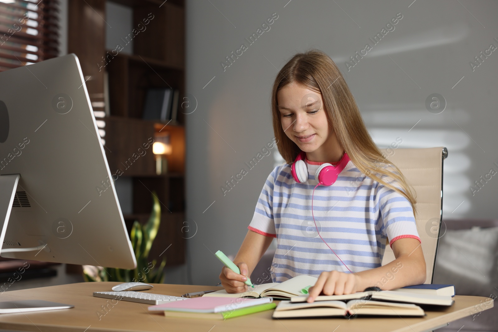 Teenage girl taking notes while studying online at table indoors Photo of Teenage girl taking notes while studying online at table indoors