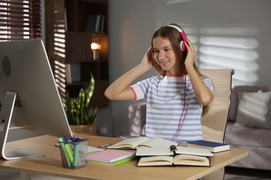 Photo of Teenage girl in headphones studying online at table indoors