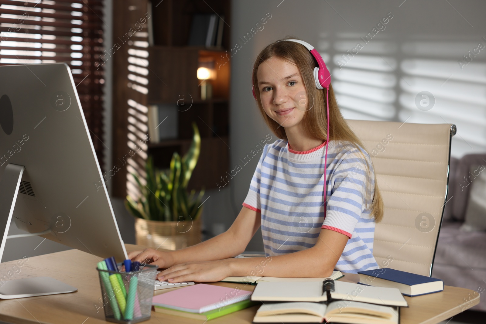 Teenage girl in headphones studying online at table indoors Photo of Teenage girl in headphones studying online at table indoors