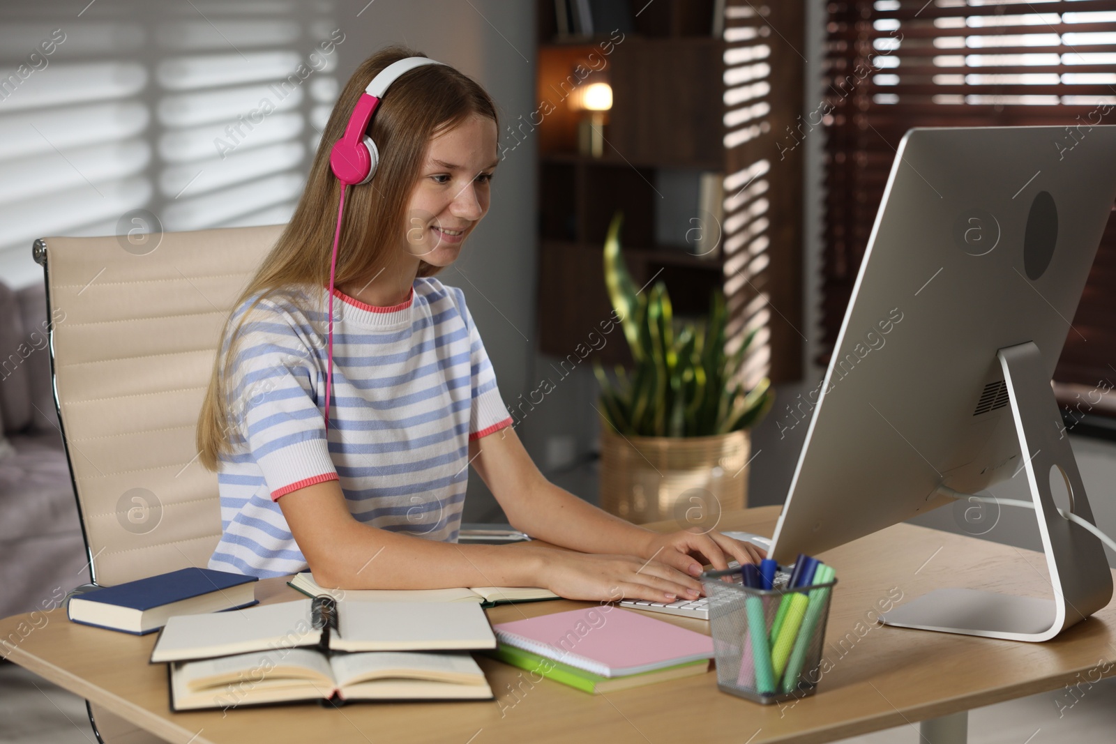 Teenage girl in headphones studying online at table indoors Photo of Teenage girl in headphones studying online at table indoors