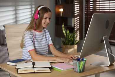 Photo of Teenage girl in headphones studying online at table indoors