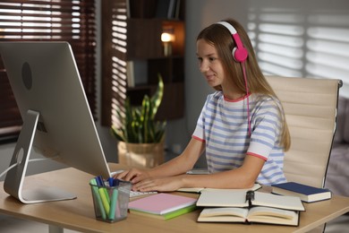 Photo of Teenage girl in headphones studying online at table indoors