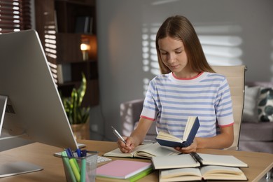 Photo of Teenage girl taking notes while studying online at table indoors
